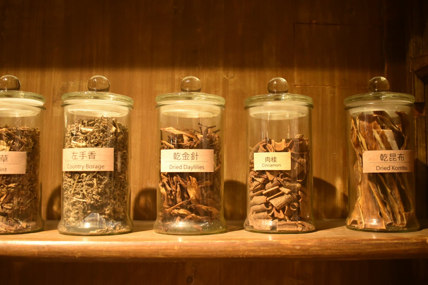 Glass jars of dried botanicals on a wooden shelf